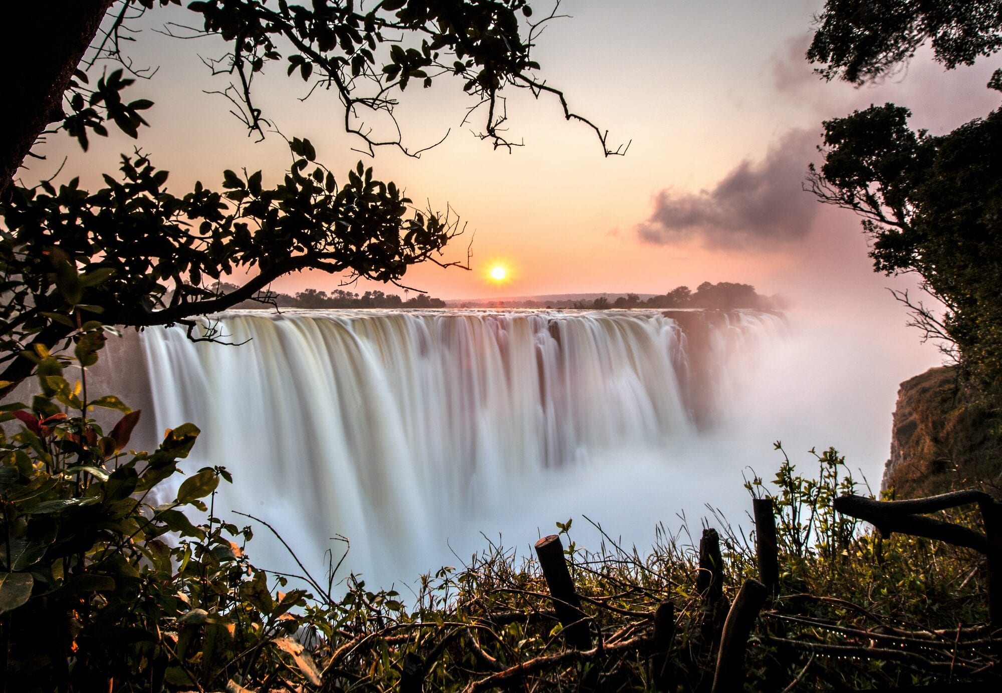 Bell 407 over the full curtain of Victoria Falls, spray rising